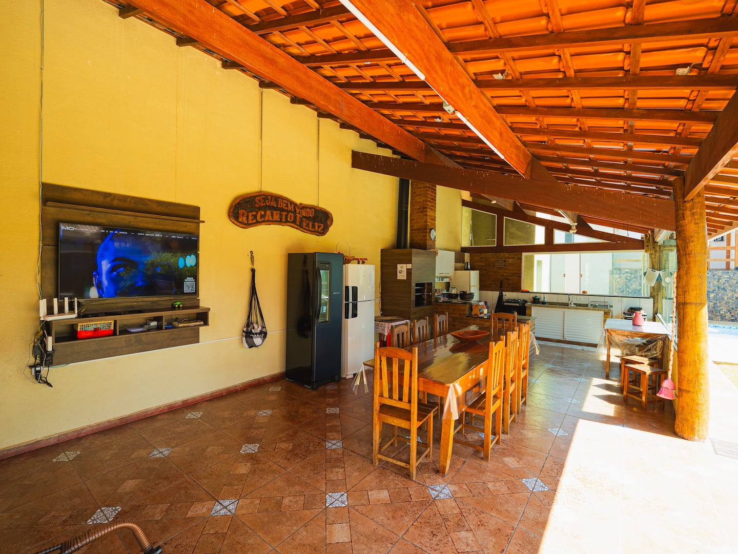 Área gourmet coberta com mesa longa, churrasqueira e vista para o jardim